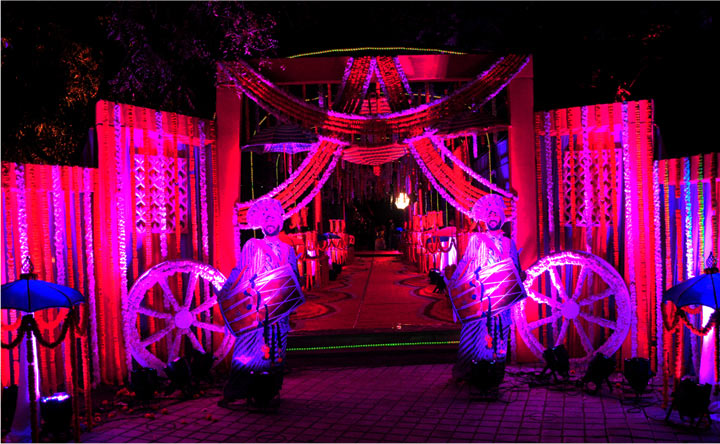 A wedding set for Bollywood filmmaking at Ramoji Film City featuring colorful lights, traditional drummers, and festive floral decorations at night.